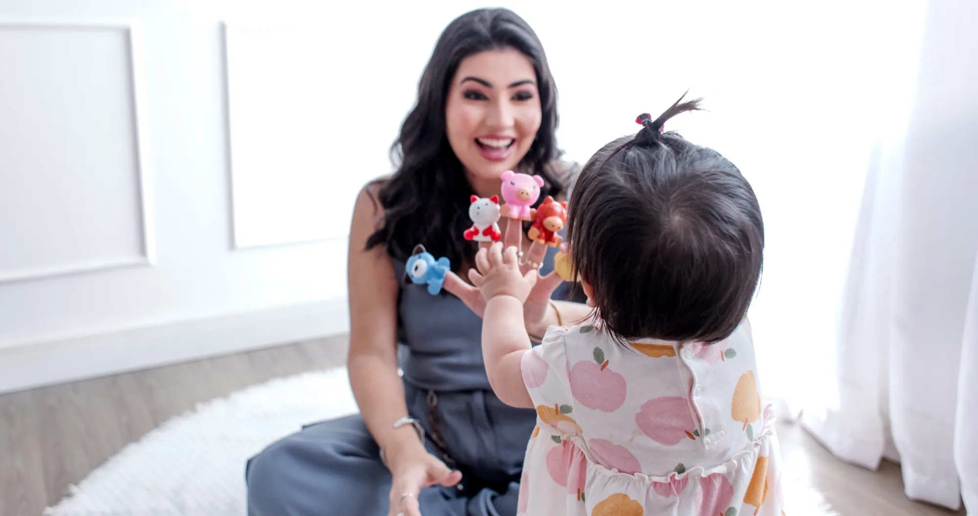 Izabella Souza brinca com fantoches de dedo diante de um bebê que estende a mão para alcançá-los