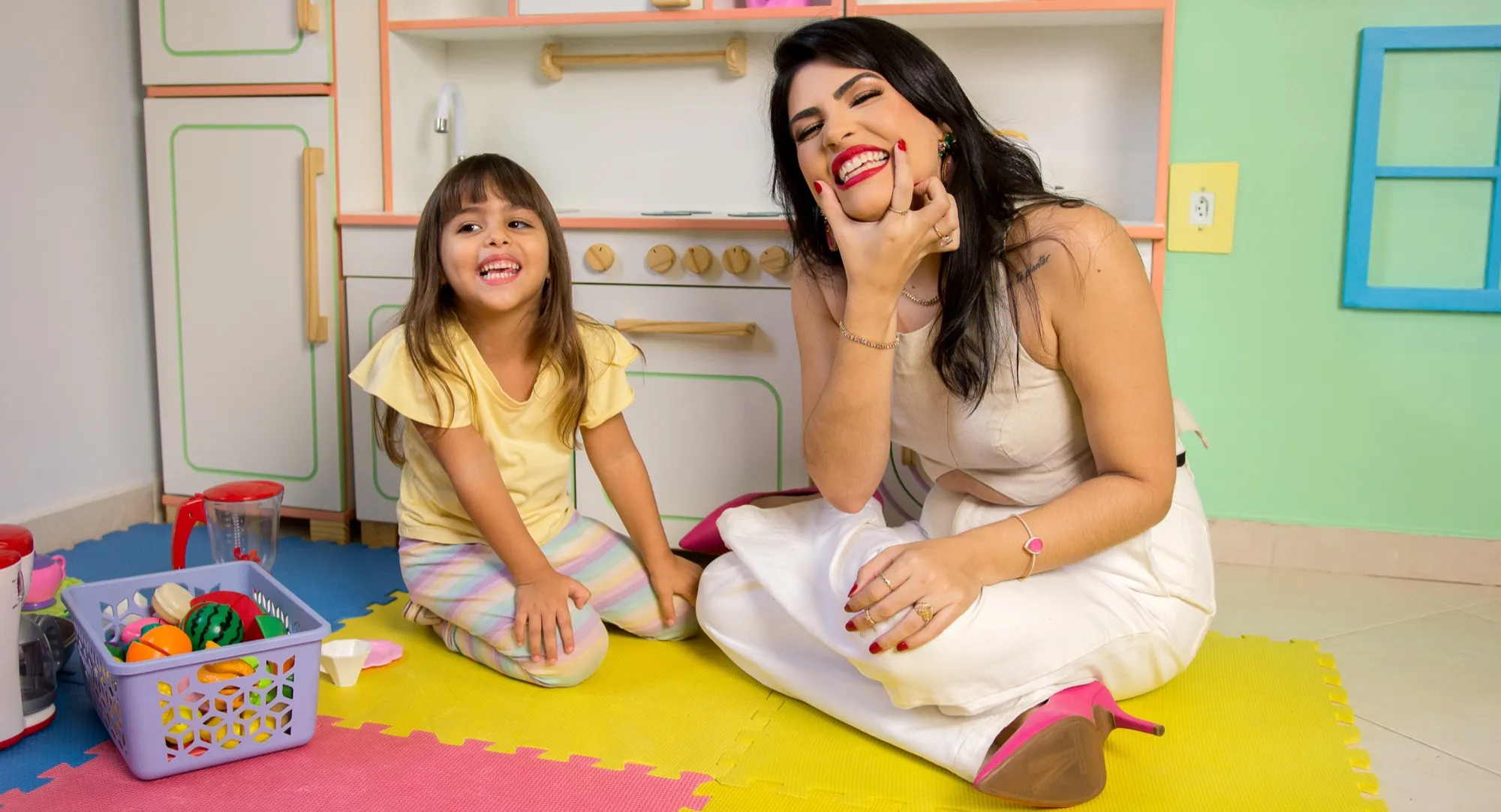 Izabella Souza e uma menina sentadas no chão da sala de brinquedos, sorrindo uma para a outra durante o atendimento